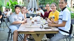 Sekelompok teman dan keluarga menikmati santapan santai di luar ruangan bersama di sebuah kafe.