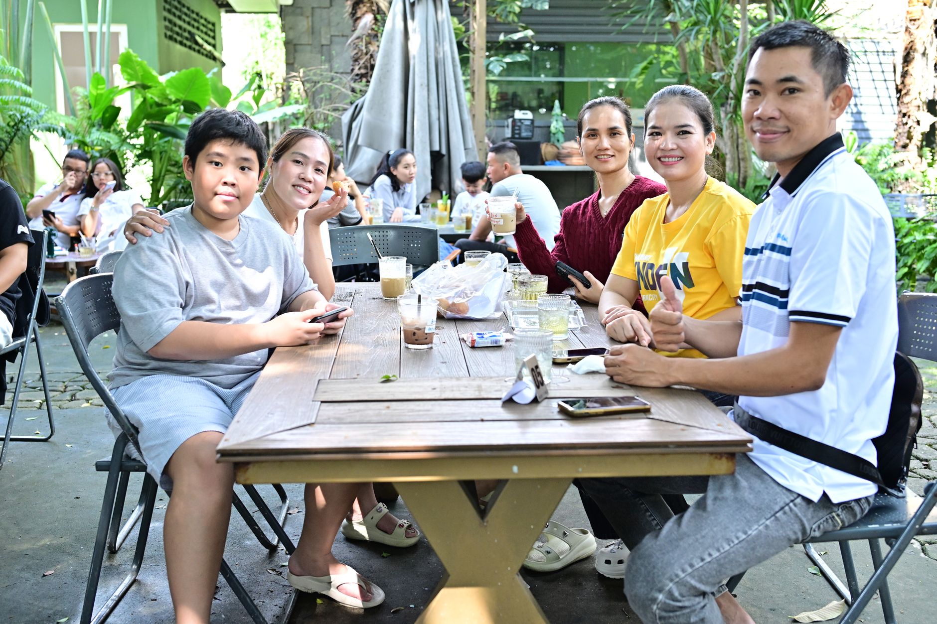 Sekelompok teman dan keluarga menikmati santapan santai di luar ruangan bersama di sebuah kafe.