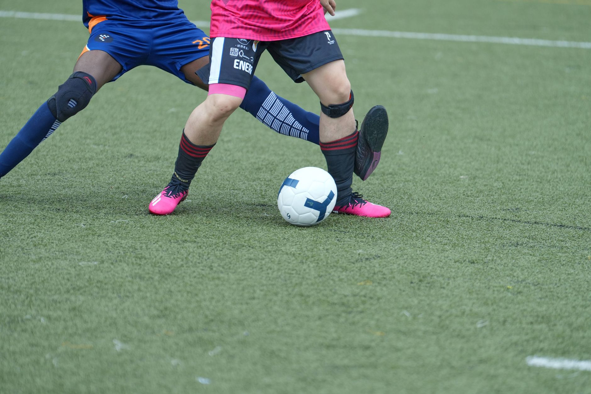 Dua pemain sepak bola bersaing memperebutkan bola di lapangan rumput selama pertandingan.