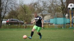 Pemain sepak bola muda yang fokus berlatih di lapangan hijau cerah di luar ruangan.