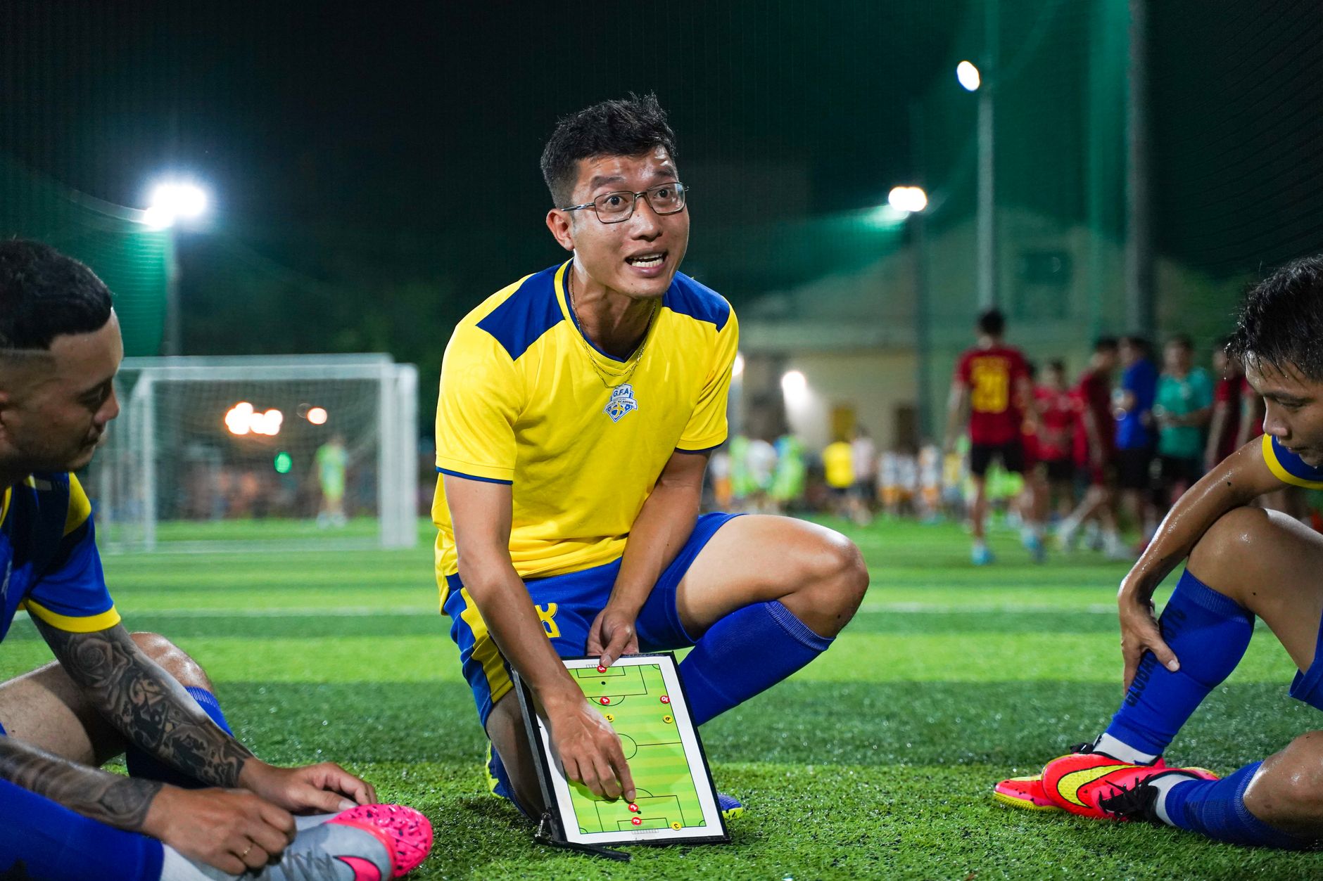 Seorang pelatih sepak bola merumuskan strategi di lapangan bersama pemain selama sesi permainan malam.