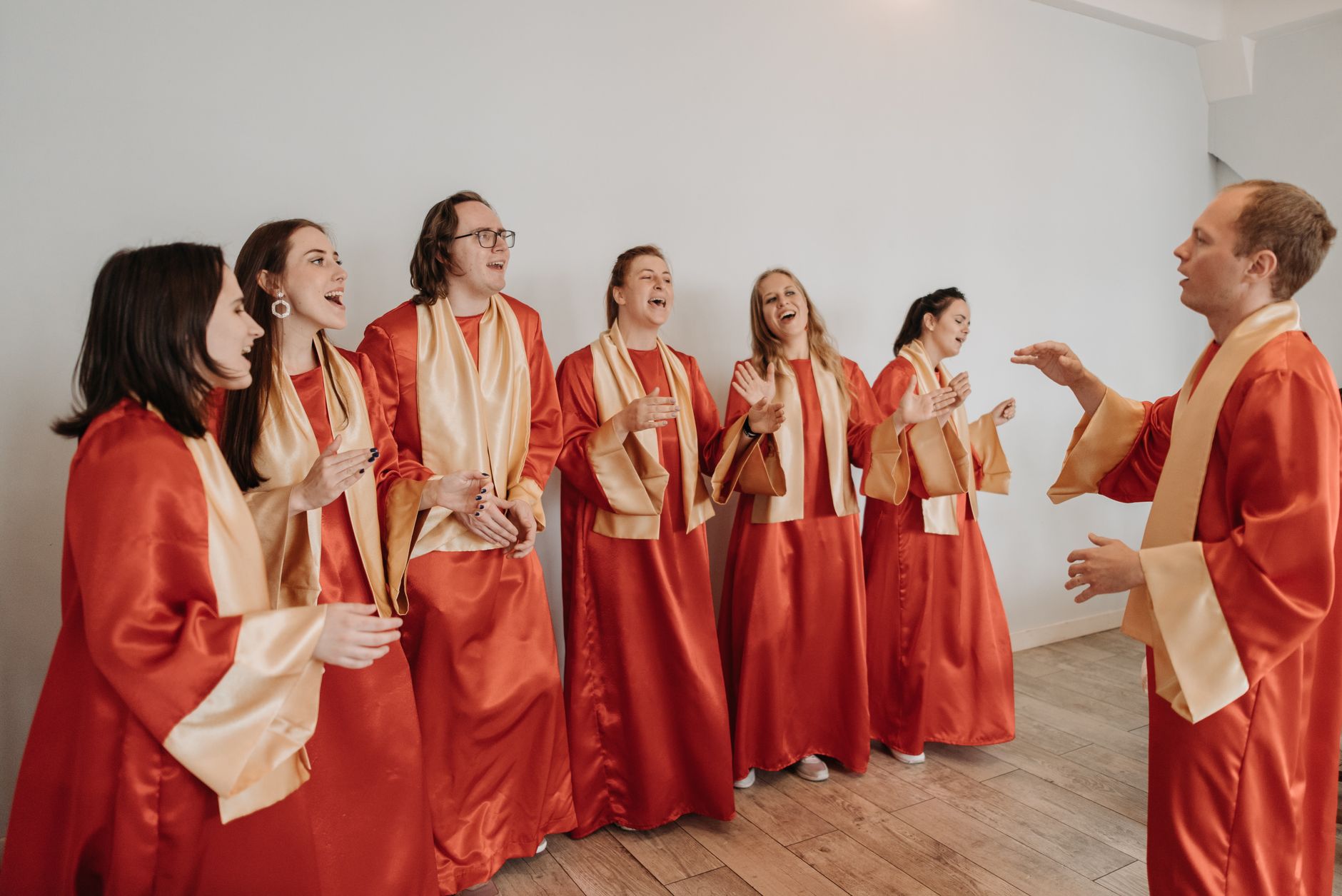 Sekelompok orang dewasa dalam gaun merah bernyanyi dengan penuh semangat di dalam ruangan, mewujudkan harmoni spiritual.