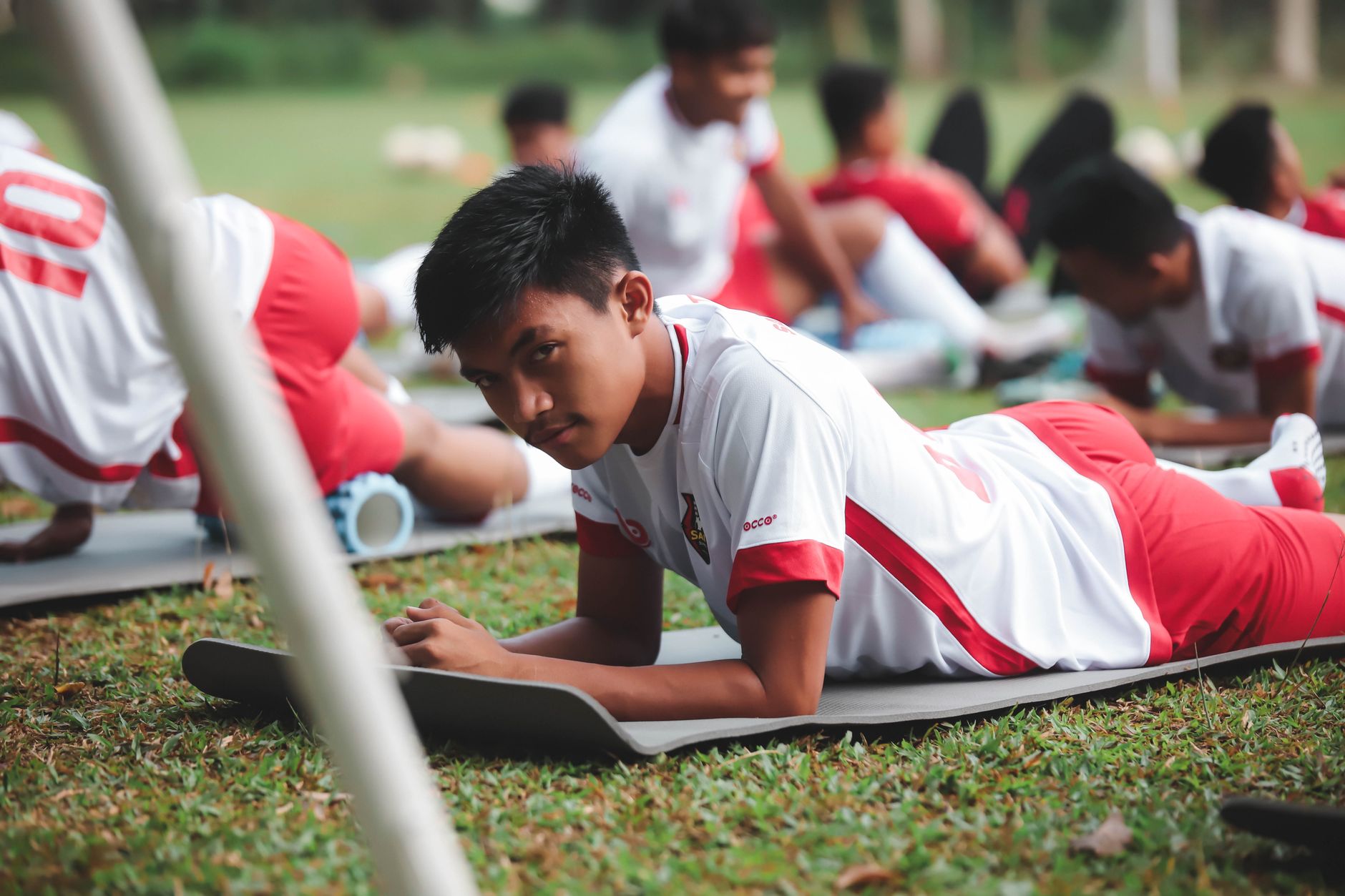 Pemain sepak bola muda yang ikut pelatihan di luar ruangan berbaring di matras latihan.