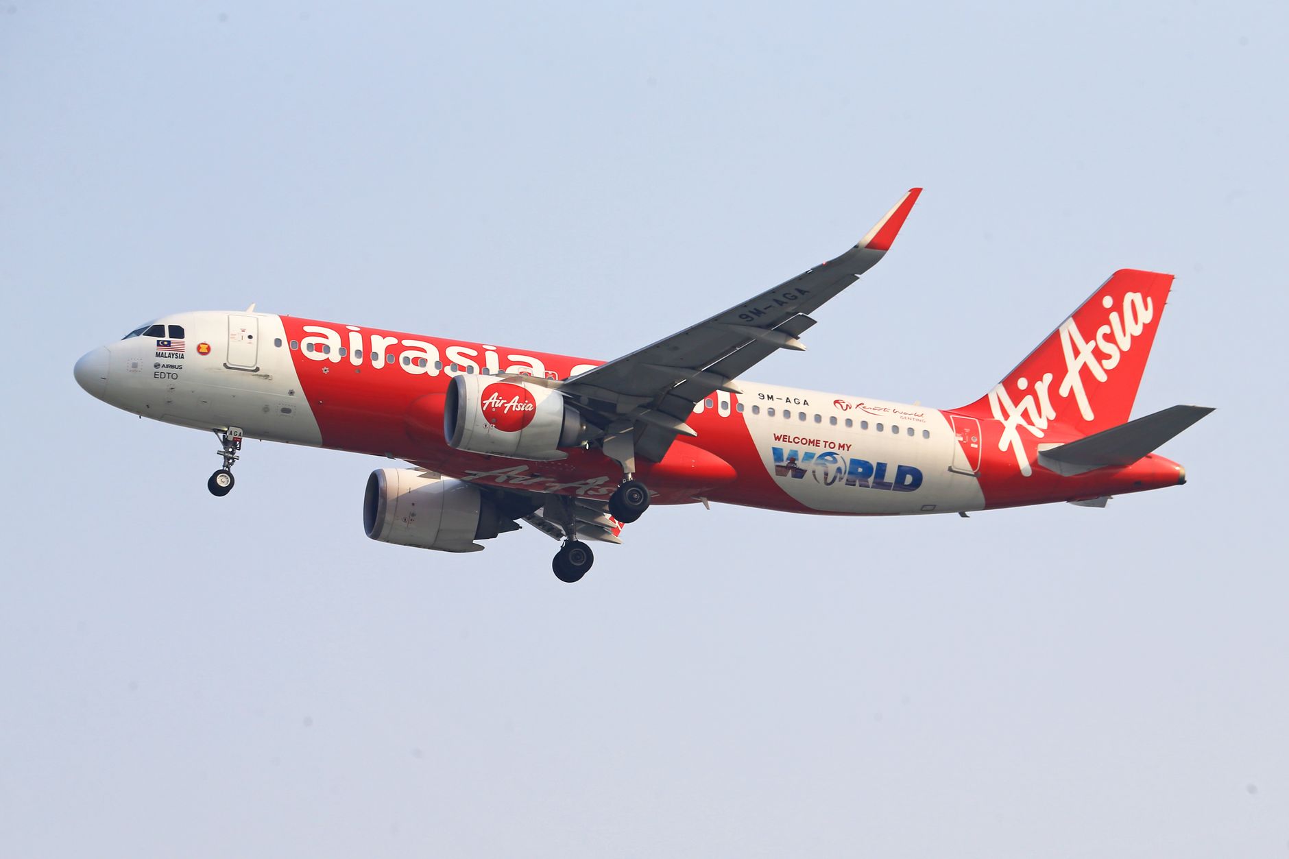 Pesawat AirAsia dalam penerbangan dengan roda pendaratan diturunkan melawan langit yang jernih.