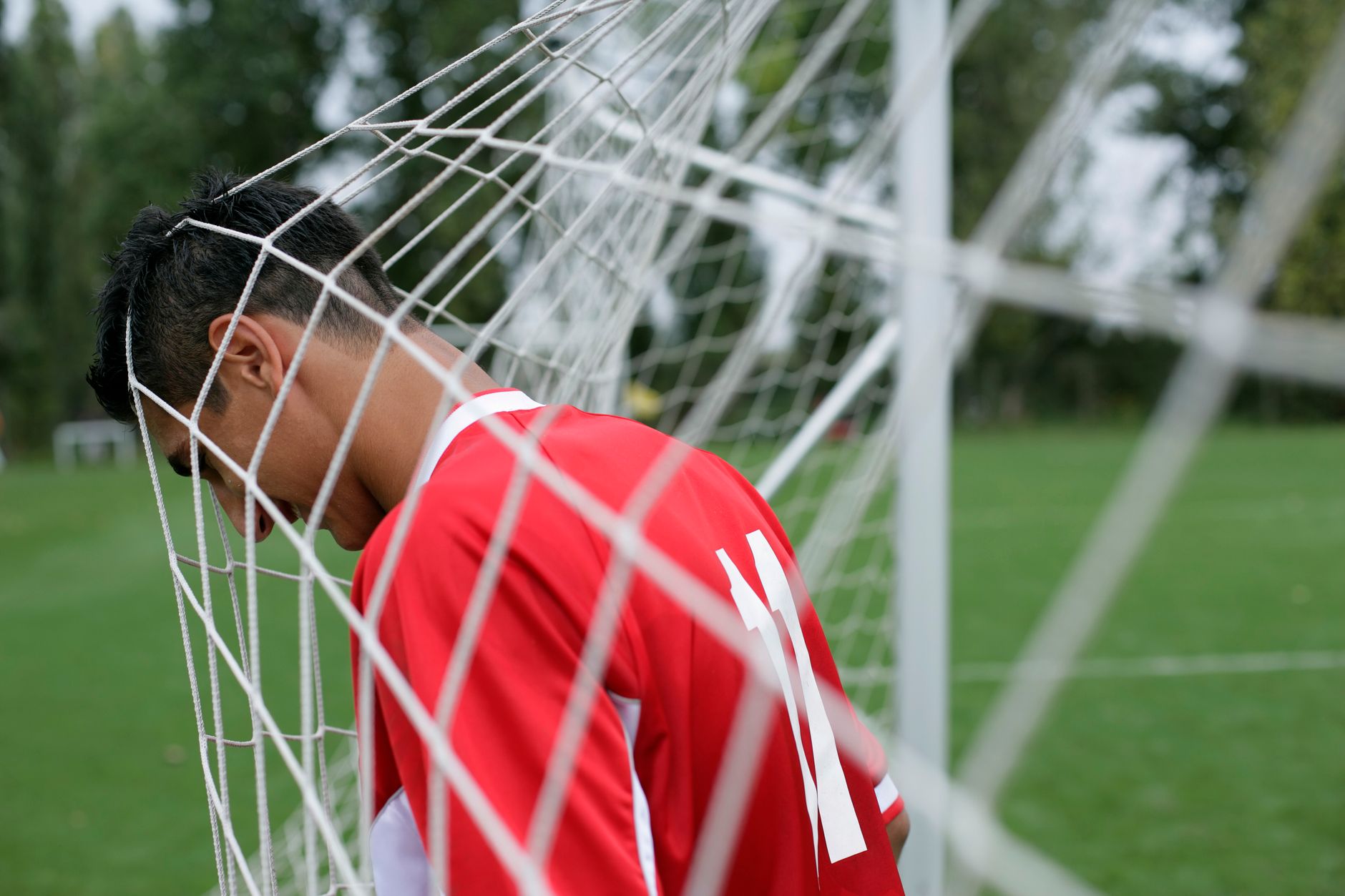 Seorang pemain sepak bola berdiri dengan kepala terjerat dalam jaring gol, mengekspresikan sikap bermain di lapangan.