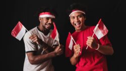 Para pemuda Indonesia bergembira merayakan dengan mengibarkan bendera, menunjukkan kebanggaan dan persatuan nasional.