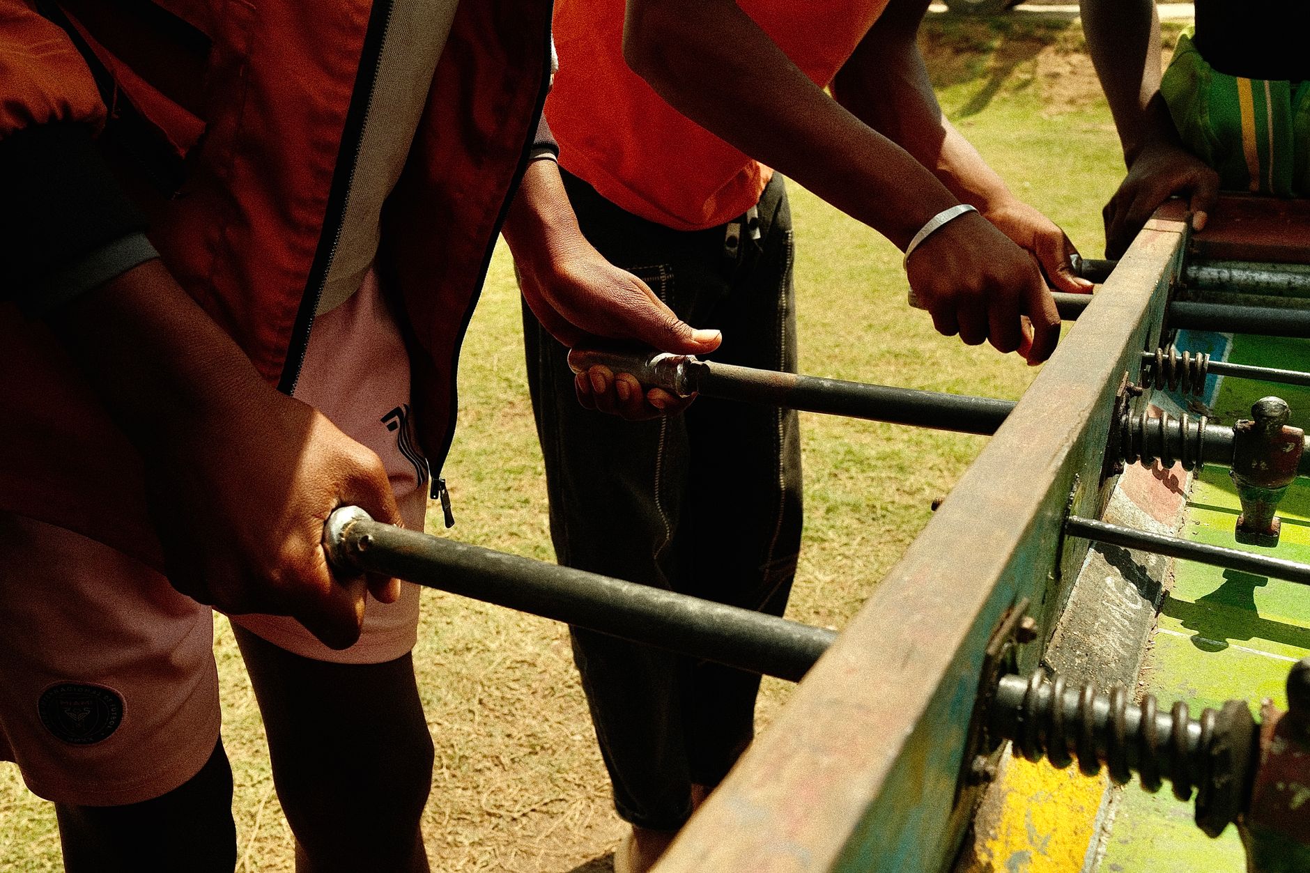 Beberapa dewasa muda terlibat dalam permainan foosball luar ruangan yang meriah di bawah sinar matahari.