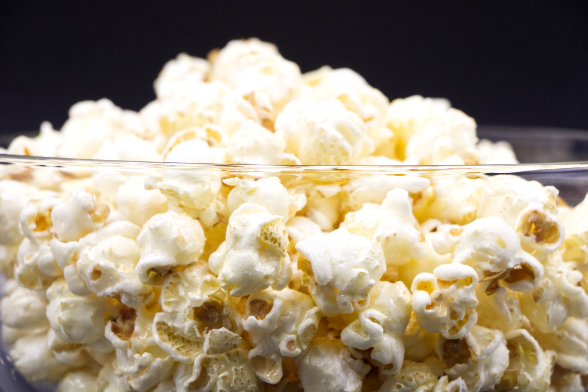 Sekumpulan popcorn yang baru saja dipopcorn dalam mangkok kaca dengan latar belakang gelap.