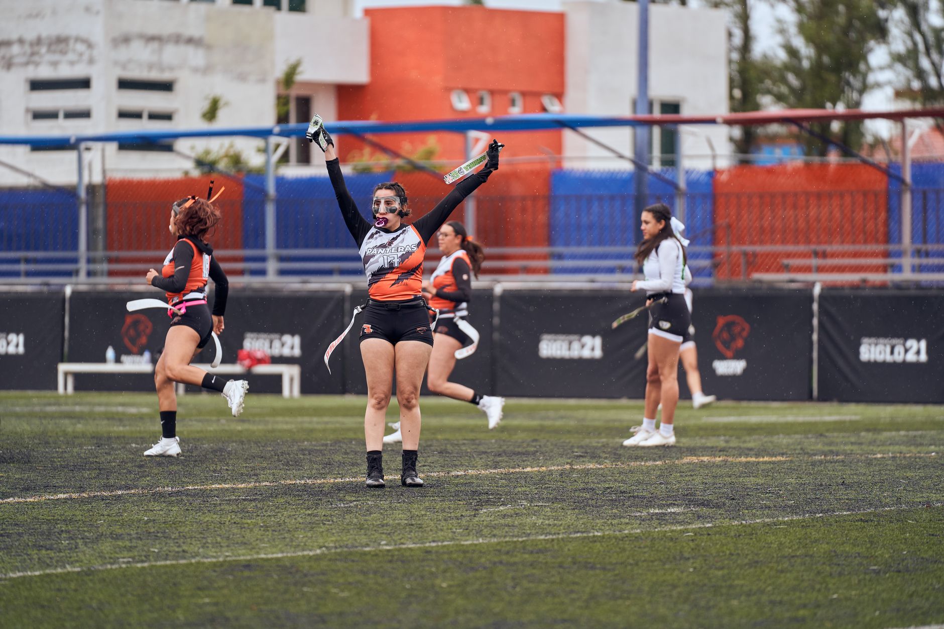 Para pemain wanita merayakan setelah mencetak gol dalam pertandingan flag football di lapangan terbuka yang semarak.