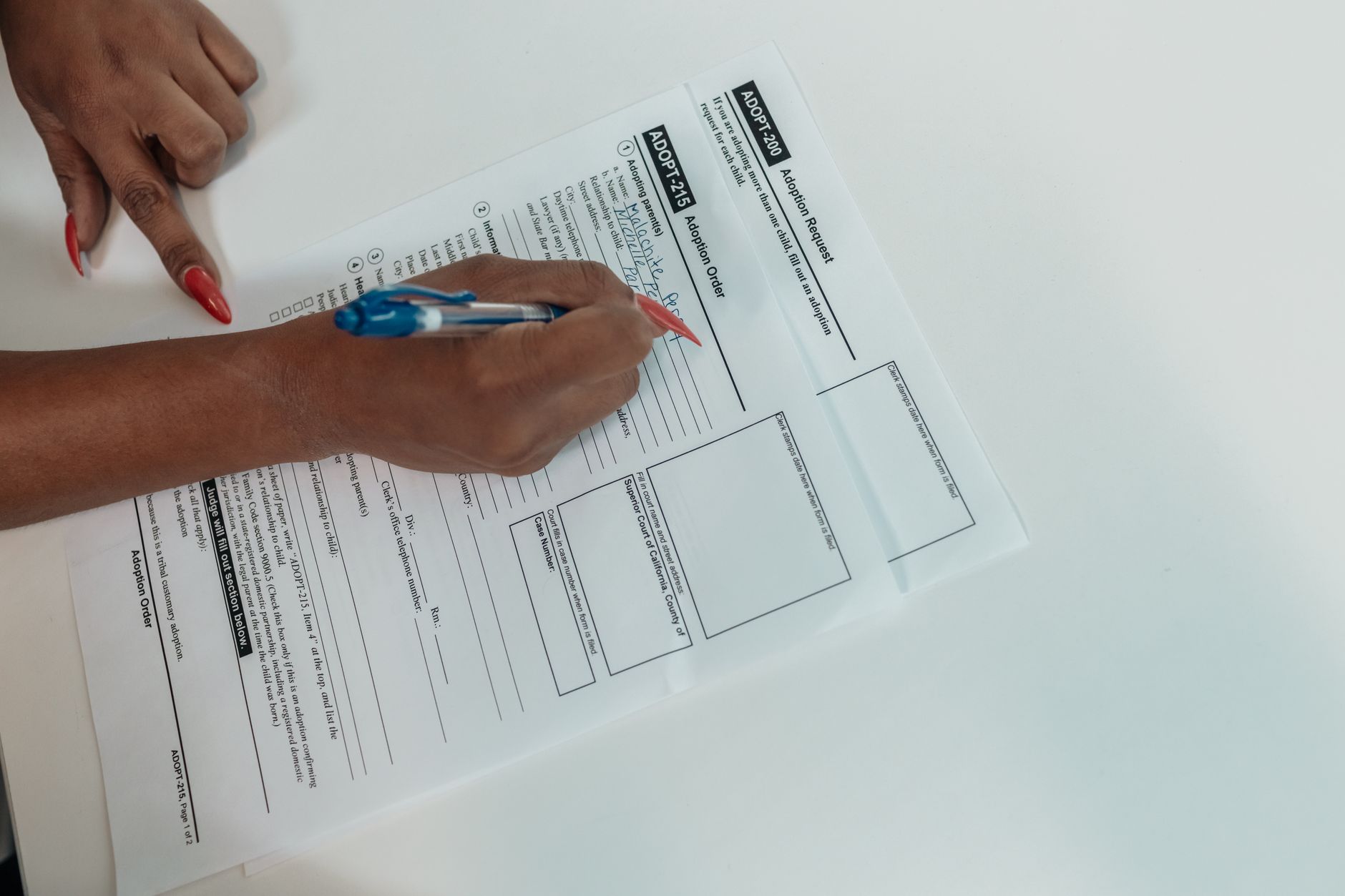 Close-up tangan yang mengisi formulir permohonan adopsi dengan pena.