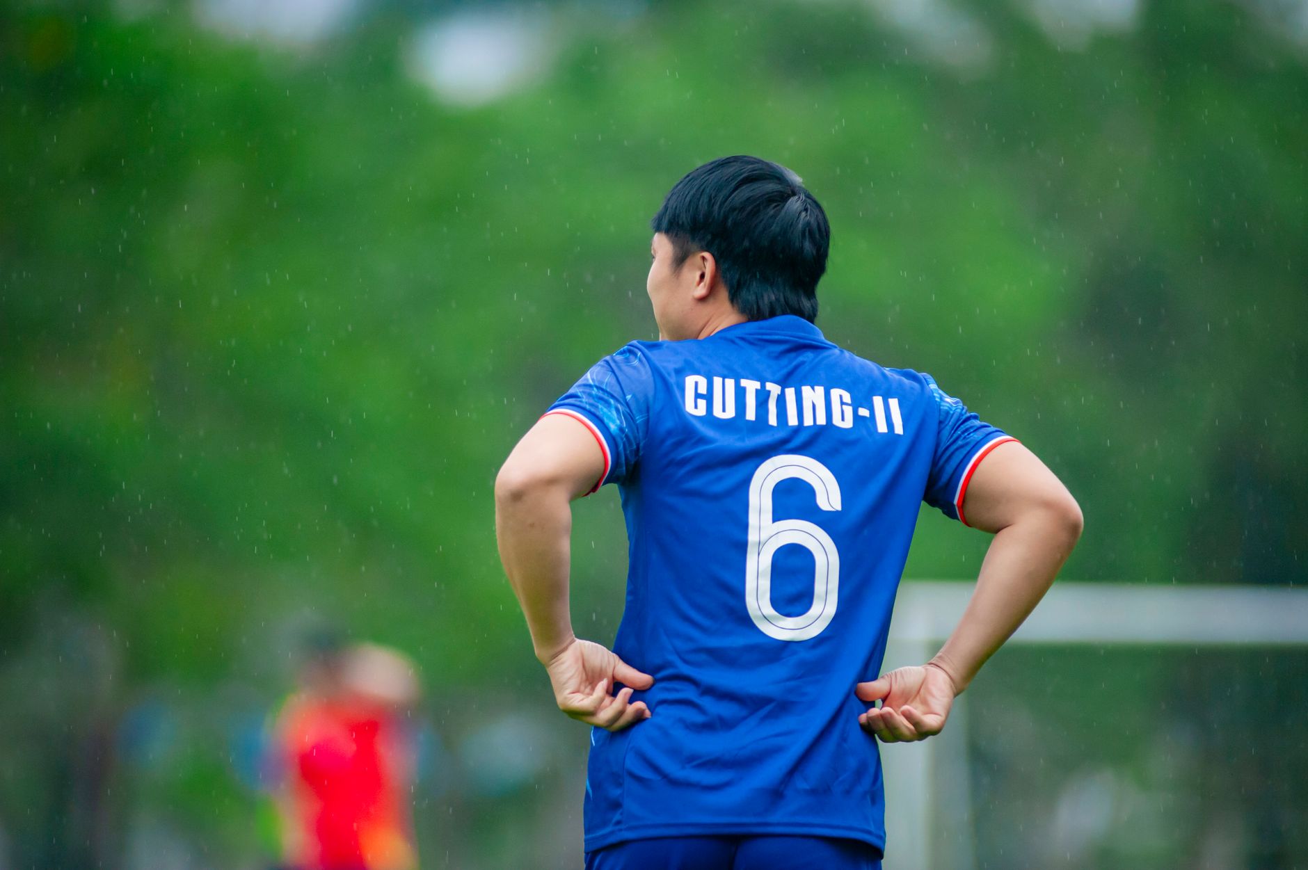 Seorang pemain sepak bola berdiri di lapangan di Hà Nội, Việt Nam, selama pertandingan yang diguyur hujan.