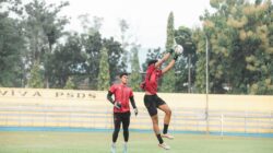 Atlet sedang bertindak selama sesi pelatihan sepak bola di luar ruangan, menampilkan lompatan energik dan kerja sama tim.