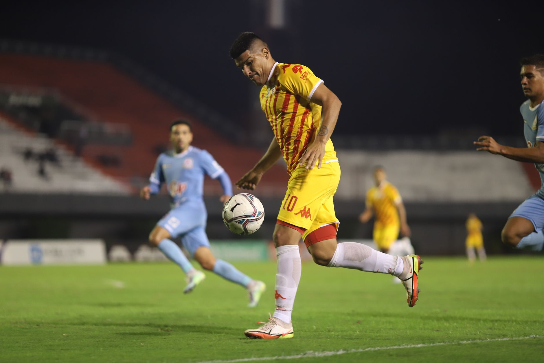 Pemain sepak bola dalam aksi selama pertandingan malam kompetitif di lapangan sepak bola yang diterangi dengan baik.