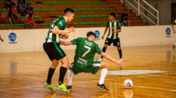 Pertandingan futsal dalam ruangan yang mendebarkan dengan atlet yang bersaing di lapangan kayu yang dipoles.