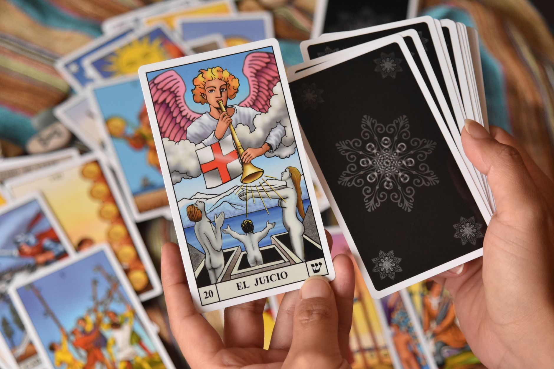 Dekatkan tangan yang memegang kartu tarot dengan kartu Penghakiman yang ditampilkan secara mencolok.