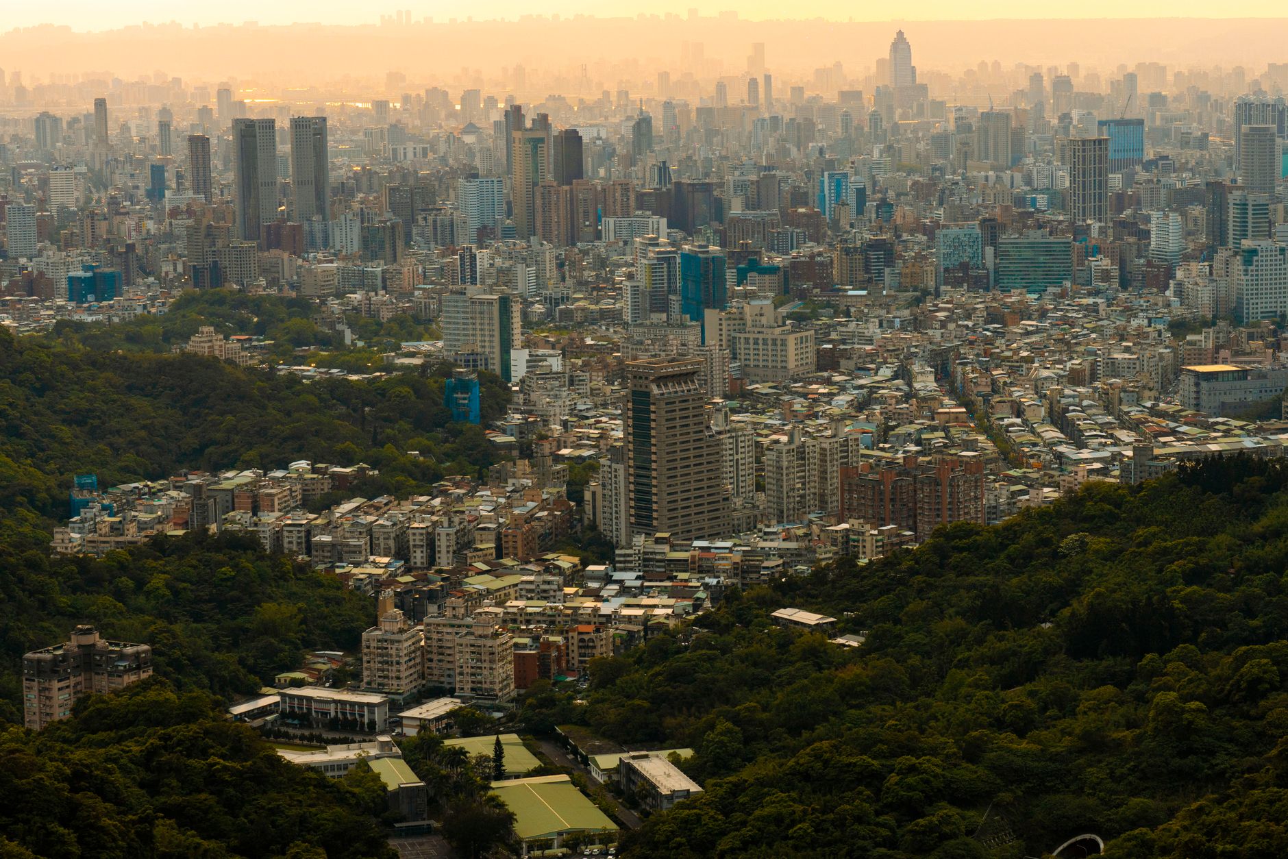 Pemandangan udara kota Taipei yang sibuk dikelilingi oleh kehijauan yang subur saat matahari terbenam.