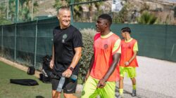 Pelatih dan para pemain menikmati sesi latihan sepak bola di luar ruangan yang cerah.