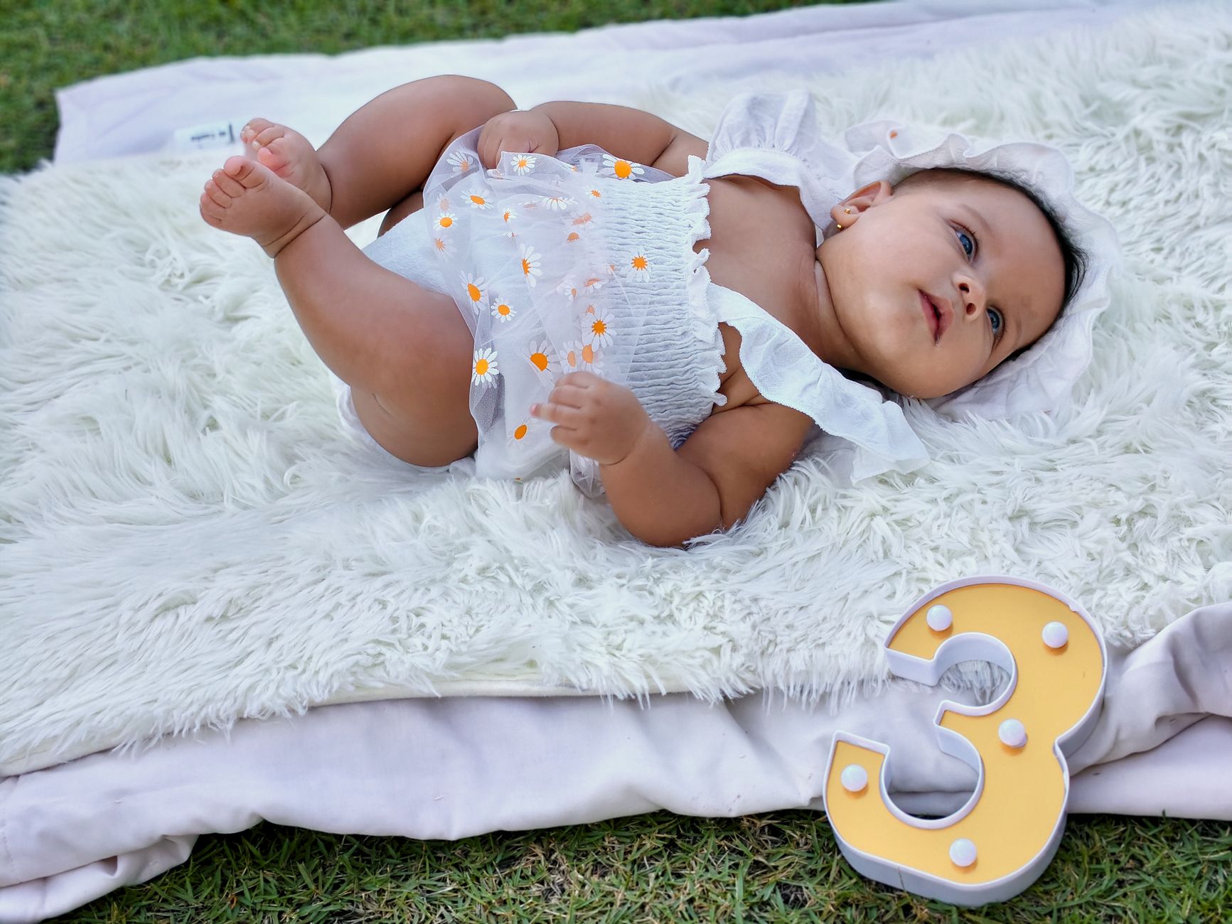 Bayi menggemaskan berbaring di atas selimut di luar ruangan, merayakan ulang bulan ketiga.