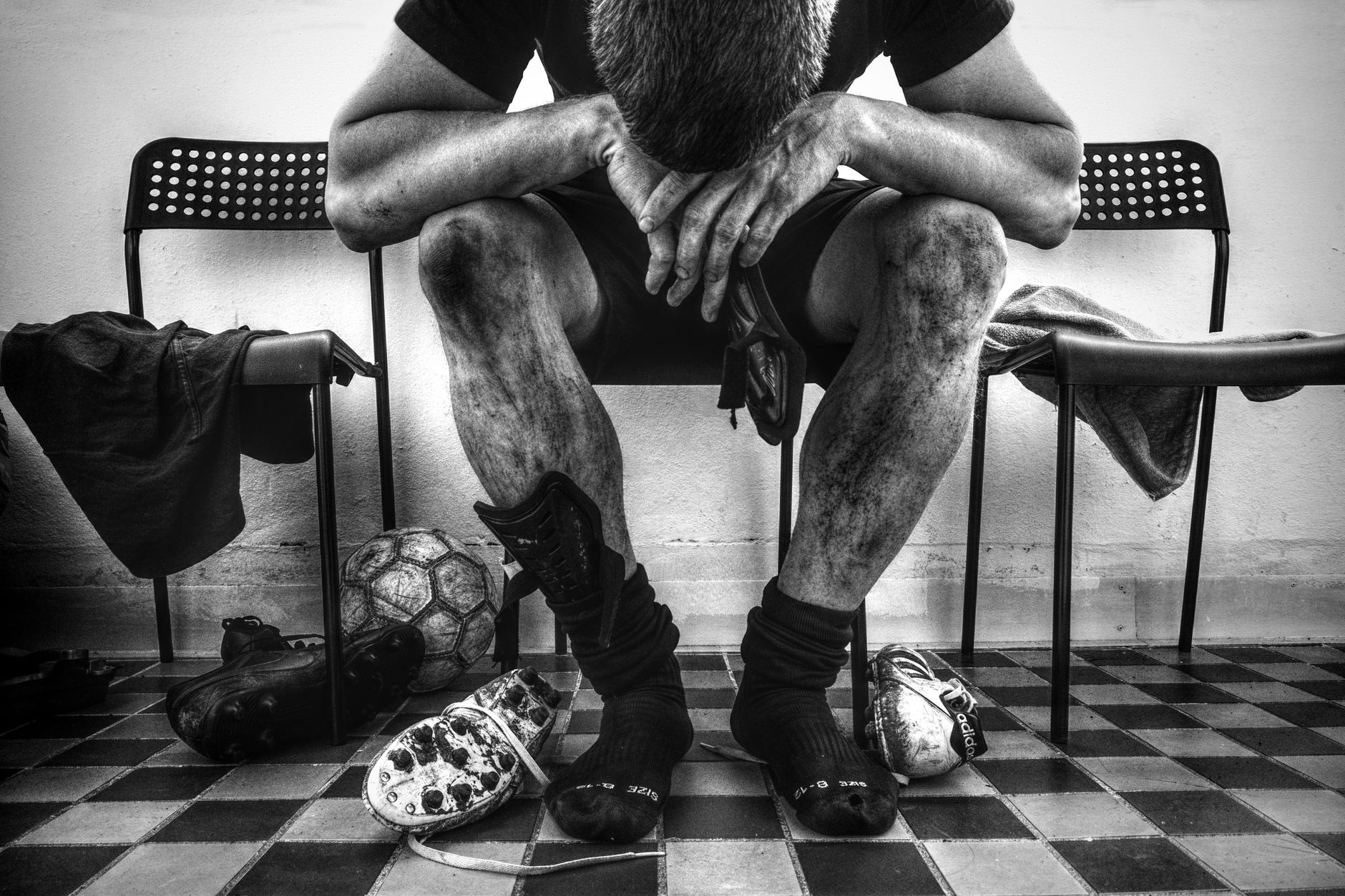 Gambar monokrom pemain sepak bola yang kelelahan beristirahat di ruang ganti.
