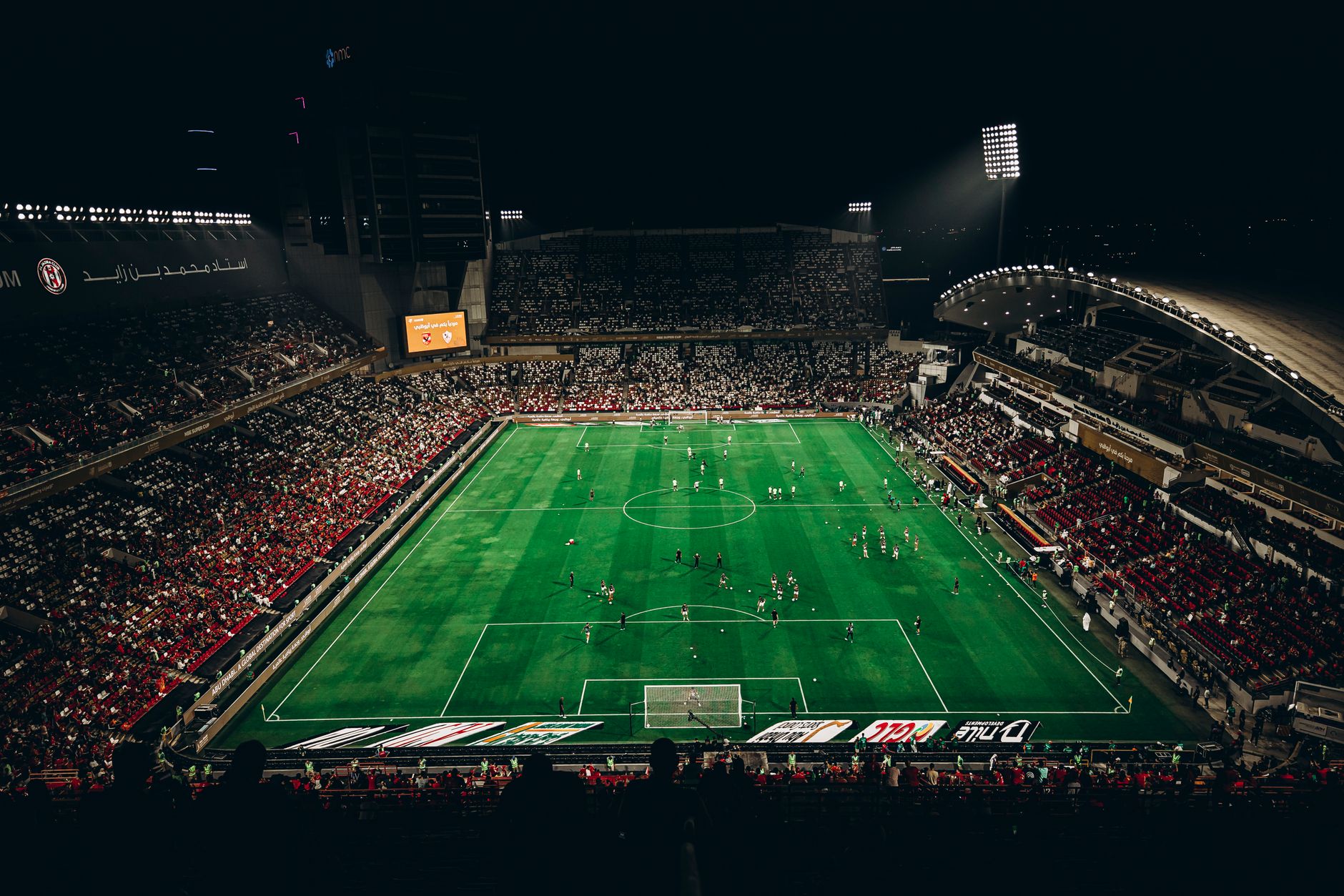Pemandangan sudut tinggi pertandingan sepak bola yang meriah dengan penggemar yang antusias di stadion besar di malam hari.