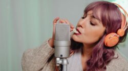 Wanita muda yang merekam konten ASMR dengan mikrofon dan headphone di dalam ruangan.