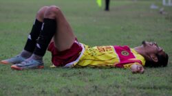 Seorang pemain sepak bola yang lelah berbaring di lapangan rumput setelah pertandingan yang intens.