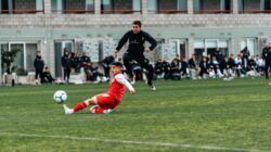 Pertandingan sepak bola penuh aksi yang menampilkan tackle geser dinamis antara dua pemain di lapangan hijau.