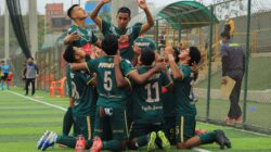 Anggota tim sepak bola remaja merayakan gol di lapangan, menunjukkan kerja sama tim dan semangat.