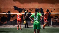 Pertandingan sepak bola wanita yang direkam di luar ruangan memperlihatkan para pemain dengan seragam berwarna cerah.