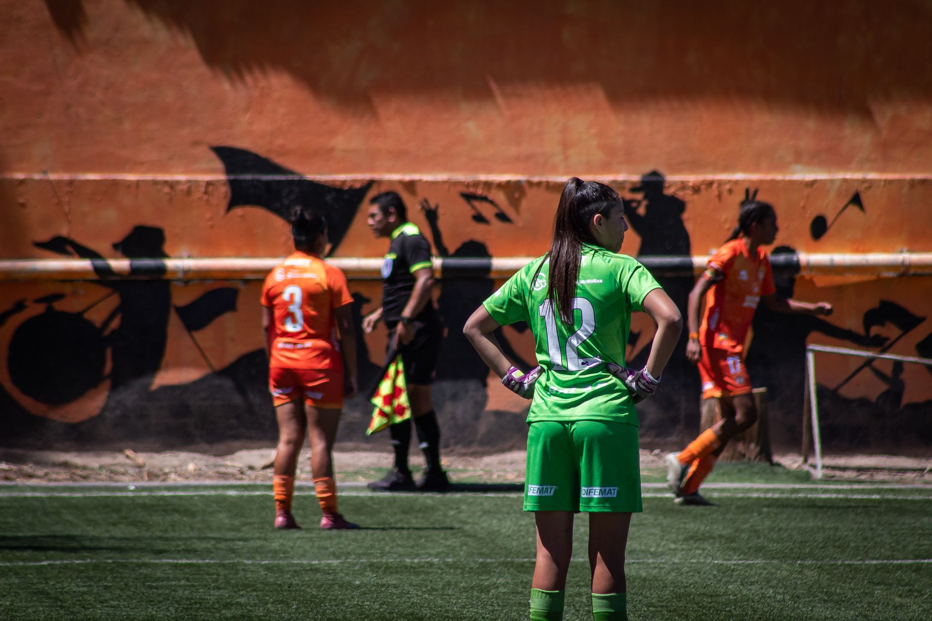 Pertandingan sepak bola wanita yang direkam di luar ruangan memperlihatkan para pemain dengan seragam berwarna cerah.