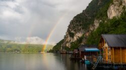 Pelangi ganda yang menakjubkan di atas danau yang tenang dengan rumah kayu di Перућац, Serbia.