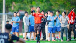 Wasit memberikan sinyal selama pertandingan sepak bola di Hà Nội dengan pemain dan penonton di latar belakang.