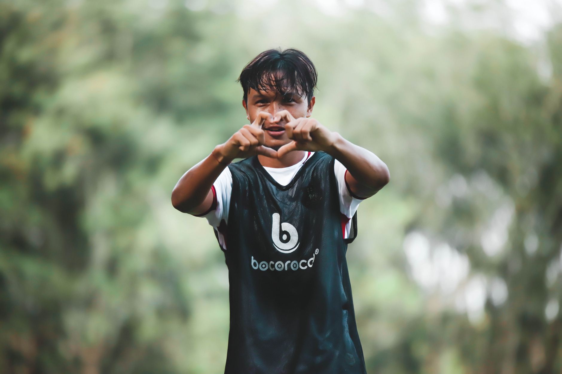 Pemain sepak bola muda yang energik membuat isyarat di lapangan, dipenuhi antusiasme dan energi.