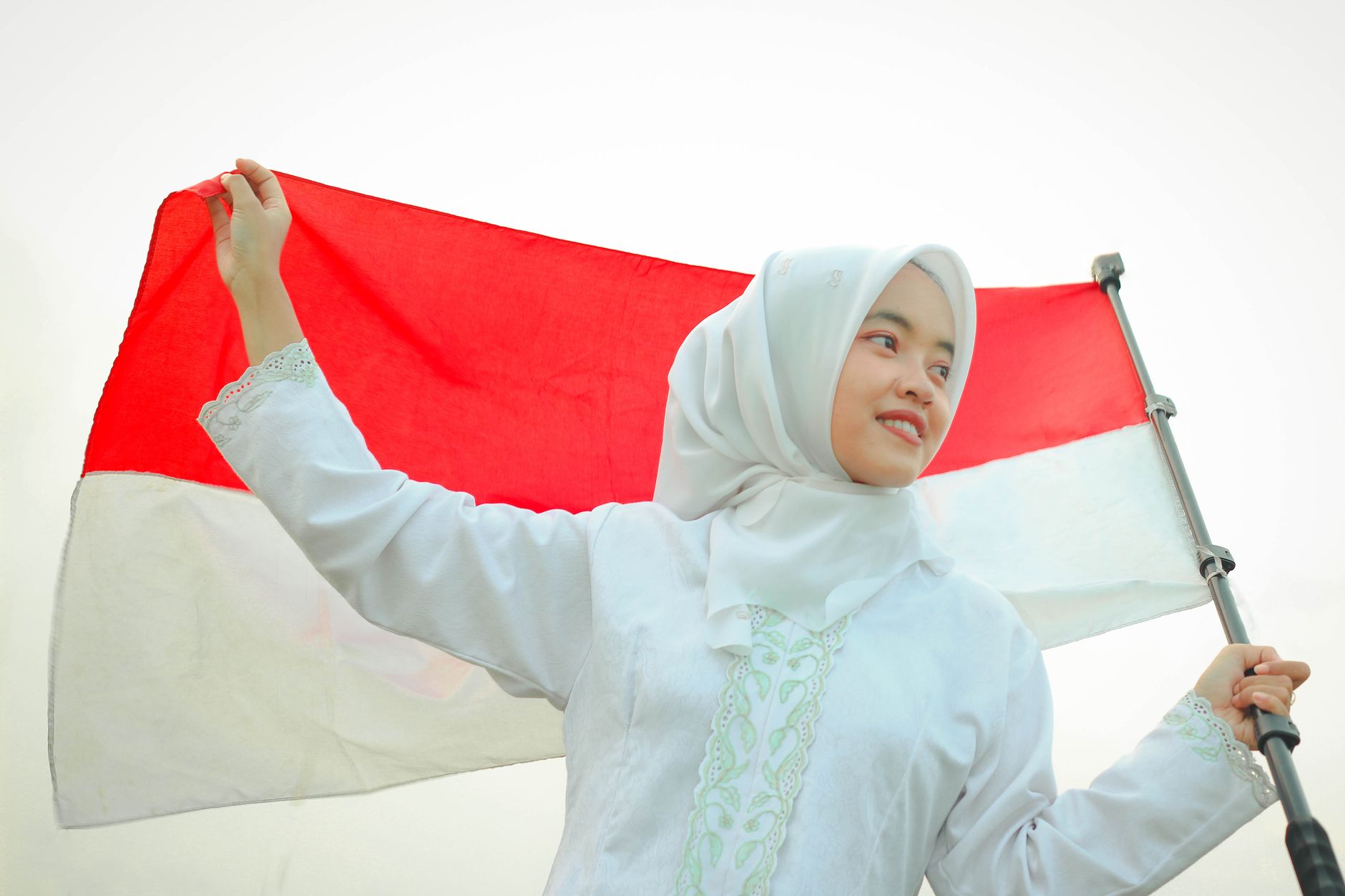 Seorang wanita muda yang tersenyum memegang bendera Indonesia, mewujudkan kebanggaan nasional.