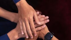 Tampilan dekat berbagai tangan yang ditumpuk bersama, melambangkan persatuan dan kerja sama tim.