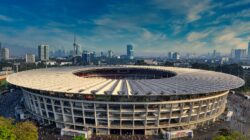 Pemandangan udara dramatis Stadion Gelora Bung Karno, Jakarta, dikelilingi oleh cakrawala perkotaan.