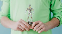 Seorang manusia memegang piala sepak bola perak di latar belakang biru.